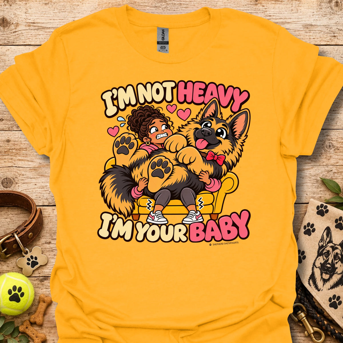 Gold T-shirt with a colorful child and dog graphic and “I'm Not Heavy I'm Your Baby” text