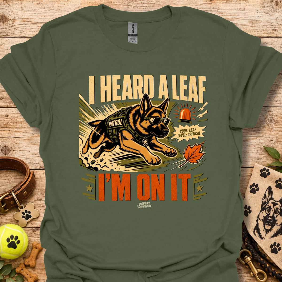 Military green t-shirt with dog leaf graphic and bold 'I HEARD A LEAF'/'I'M ON IT' text.