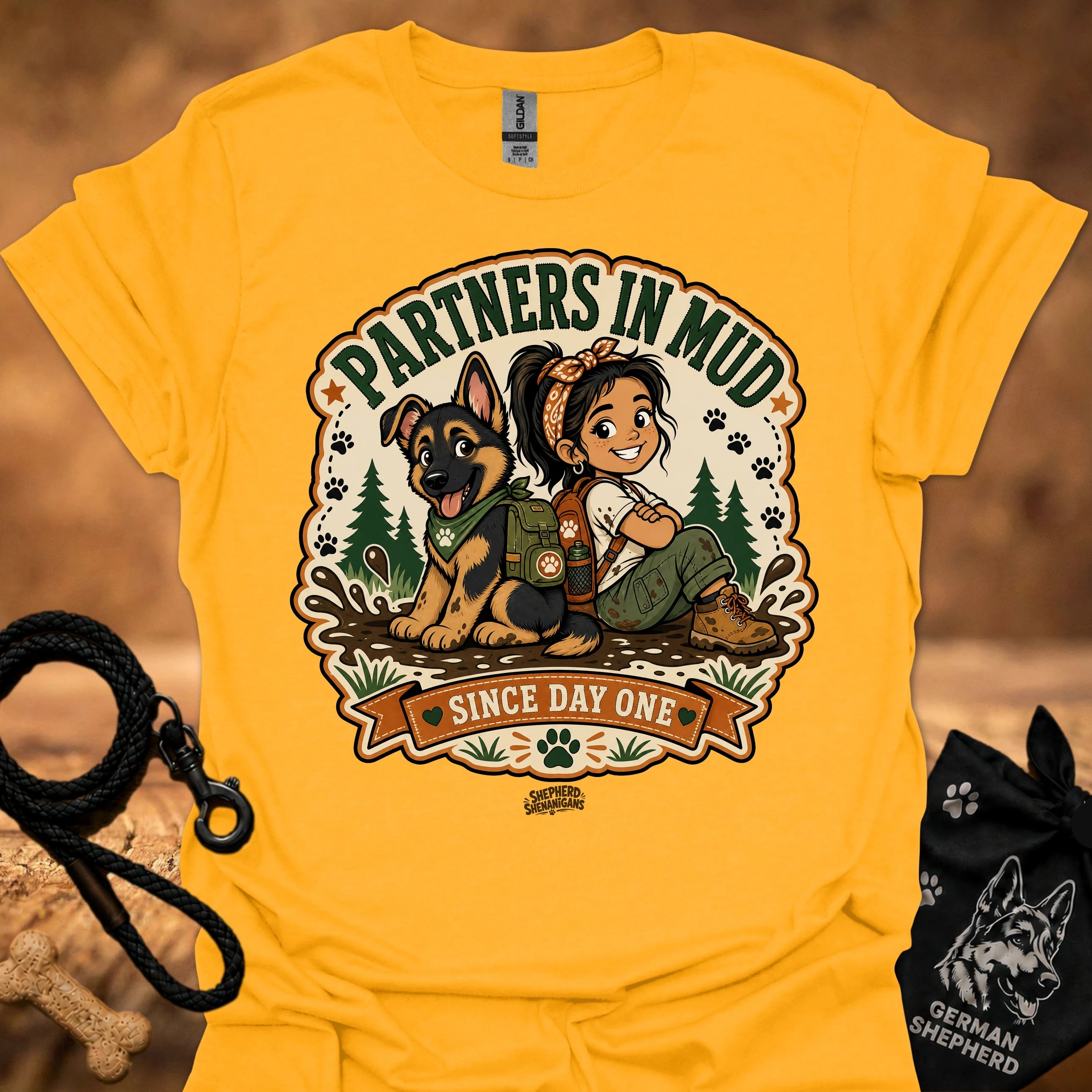 Gold women’s t-shirt with “Partners in Mud” dog and girl “Since Day One” graphic