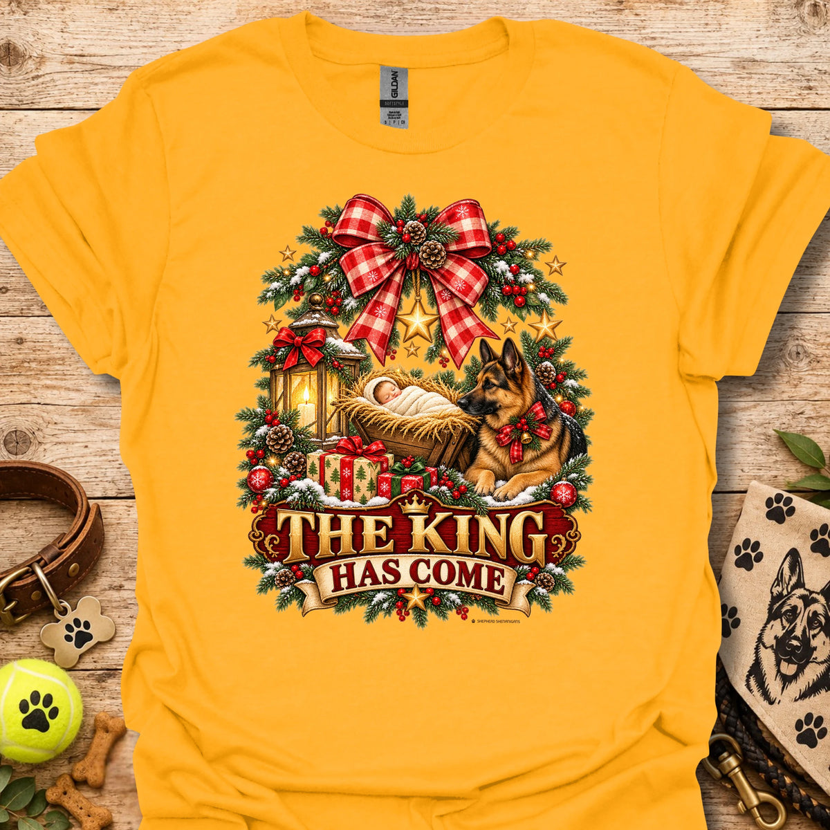 Gold holiday graphic T-shirt with wreath, dog, and “THE KING HAS COME” print