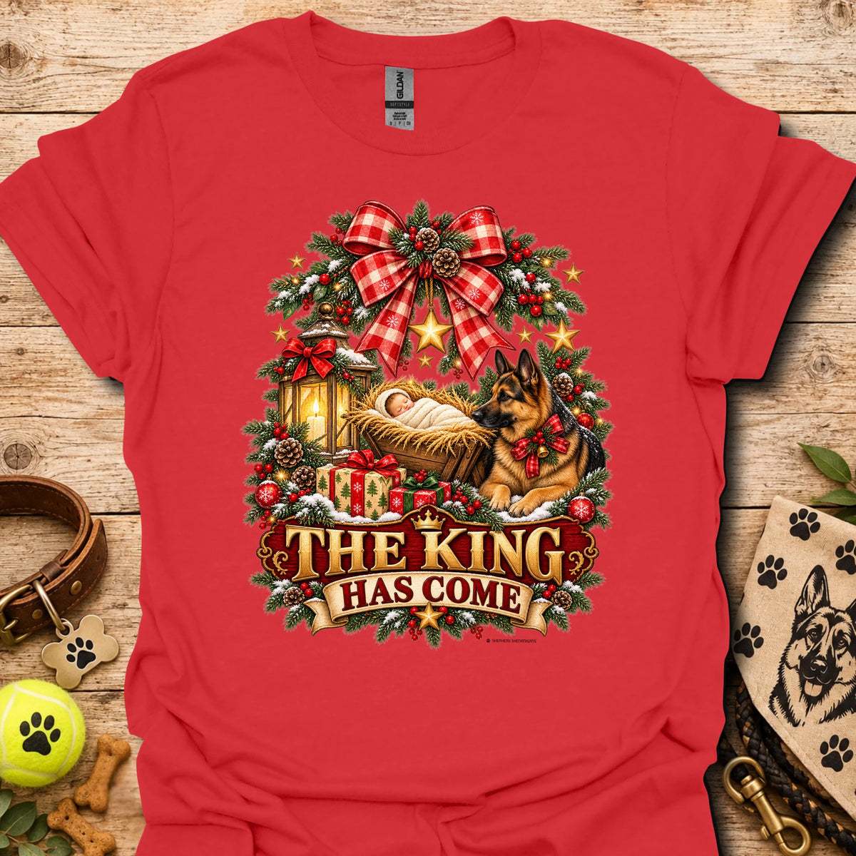 Red holiday graphic T-shirt with wreath, dog, and “THE KING HAS COME” print